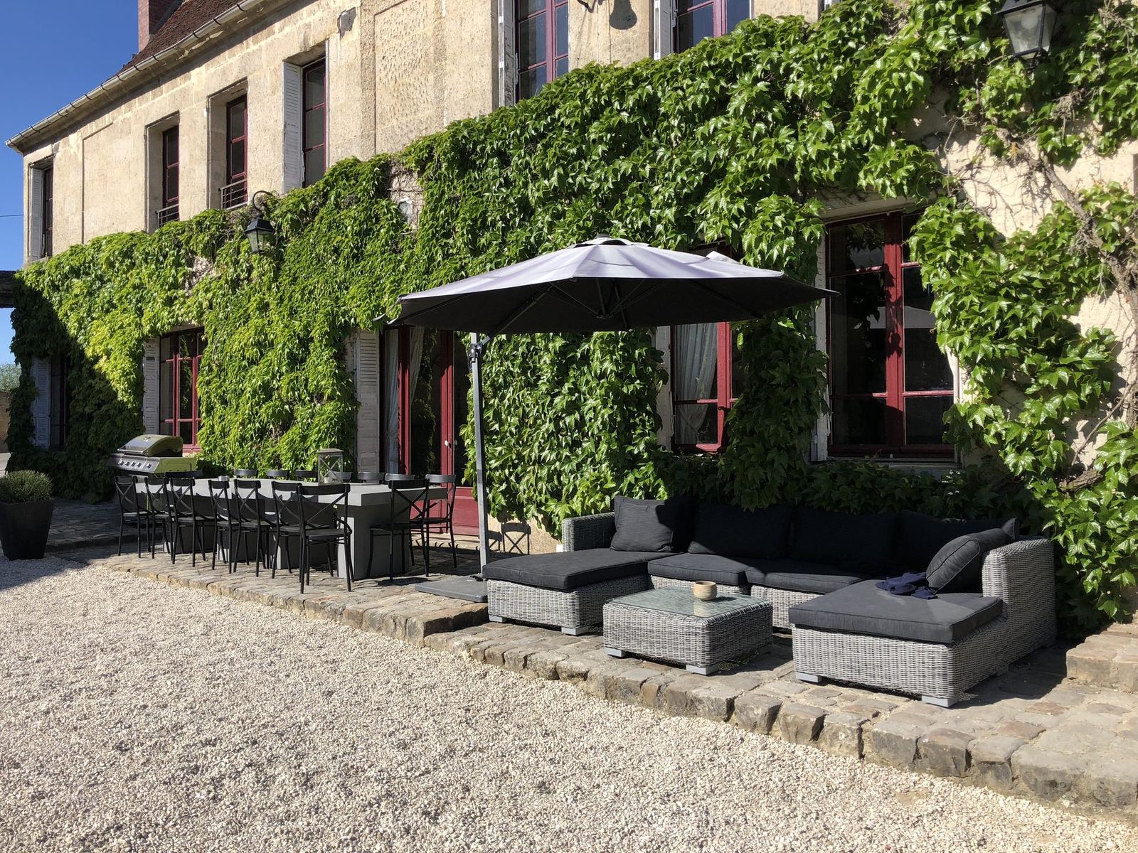 La façade de L’Instant La Ferme sous la vigne vierge, avec son salon de jardin