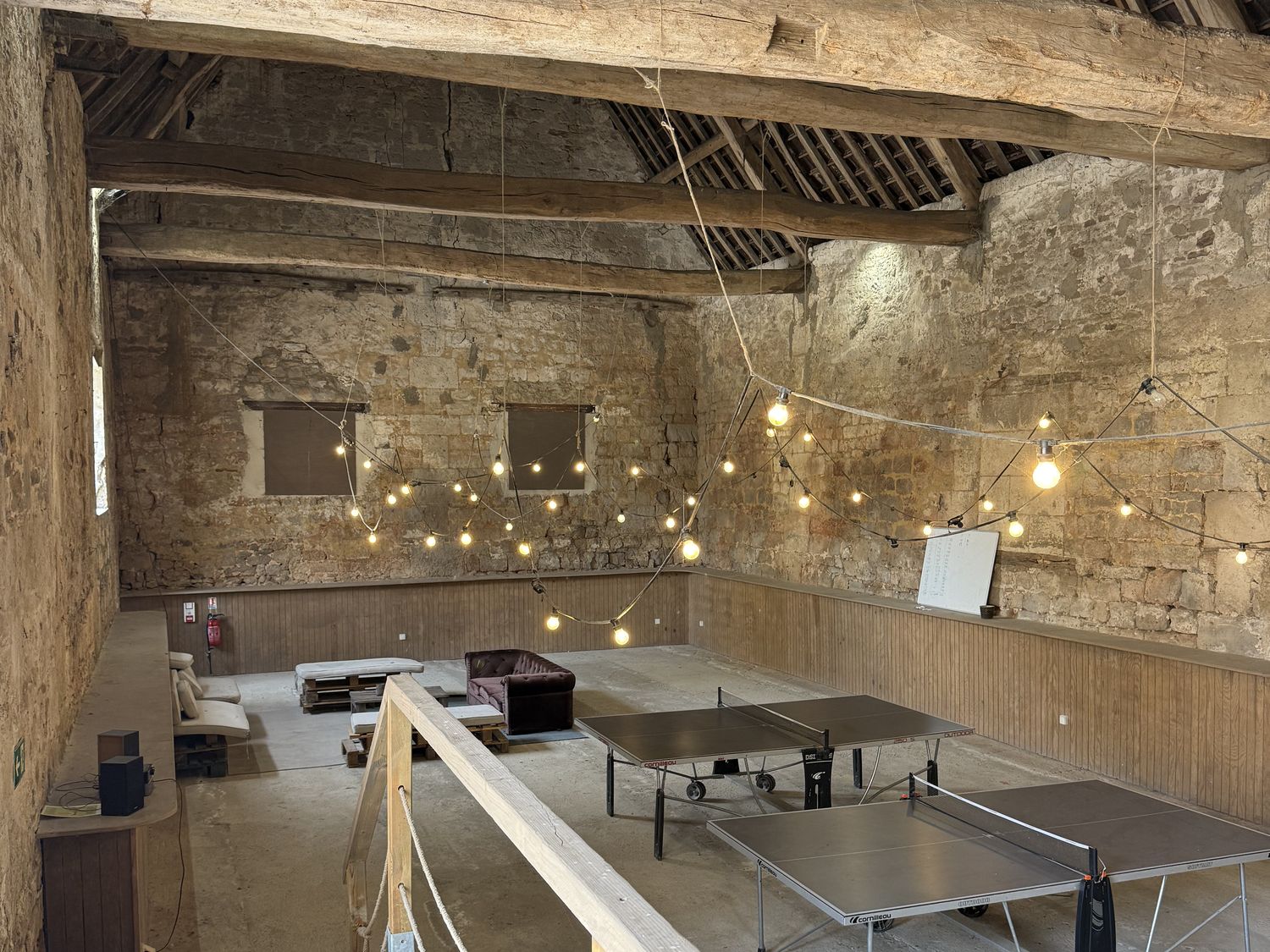 La grange : murs de pierre, poutres de chêne, guirlandes et tables de ping-pong