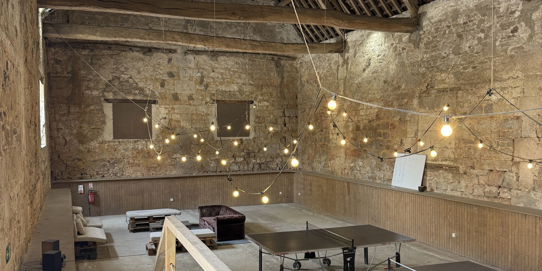 L’intérieur de la grange : murs de pierre, poutres de chêne et guirlandes lumineuses