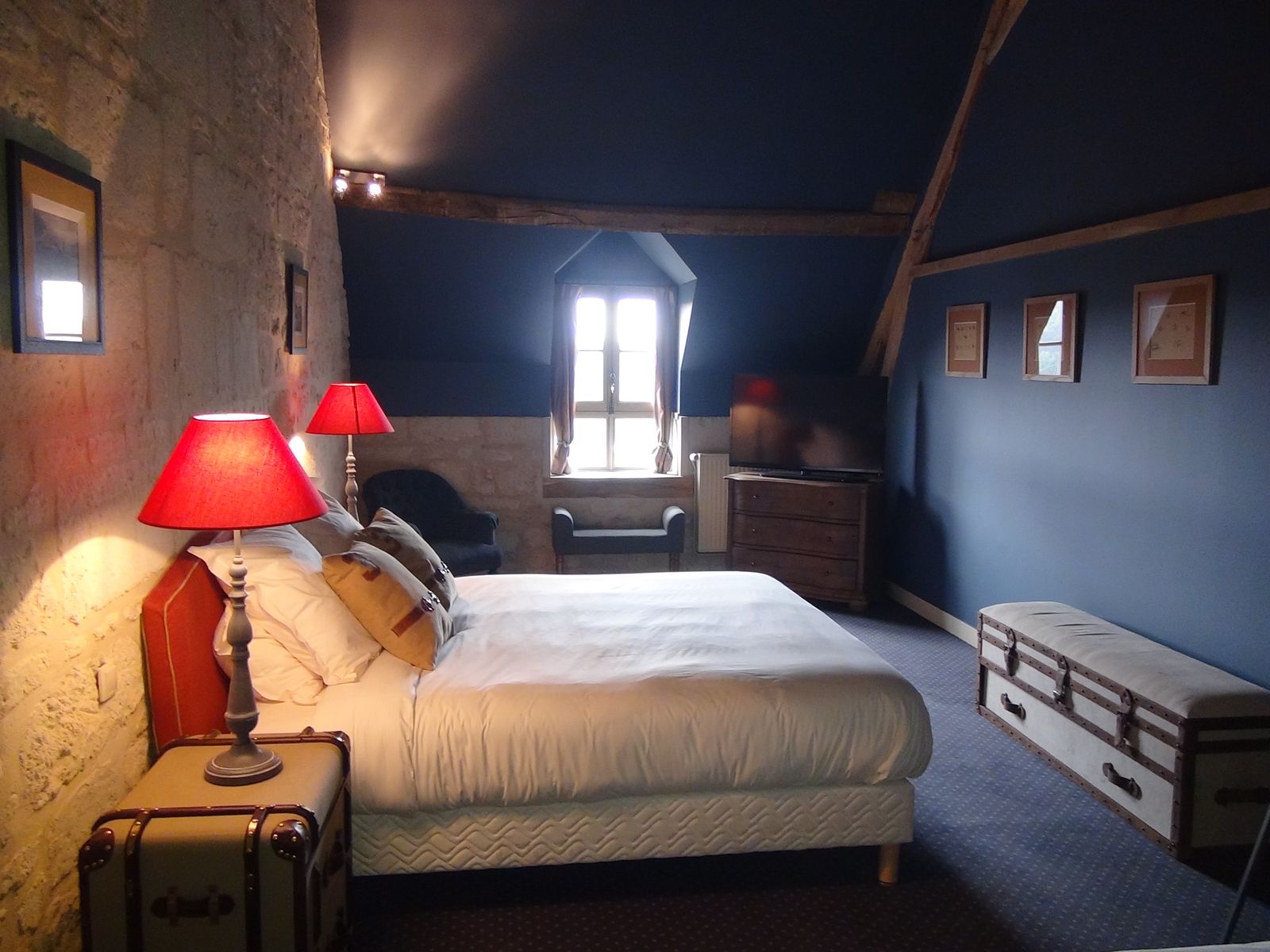 La chambre sous les combles : mur de pierre, bleu profond, abat-jour rouges
